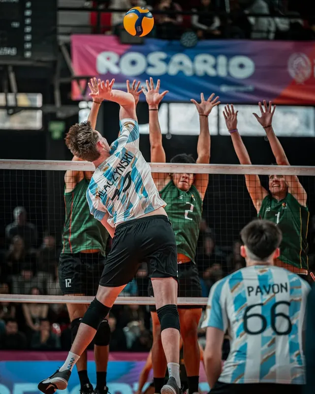 Leandro Klaczynski salta para atacar ante el bloqueo de tres jugadores de Bolivia, con un cartel de Rosario de fondo