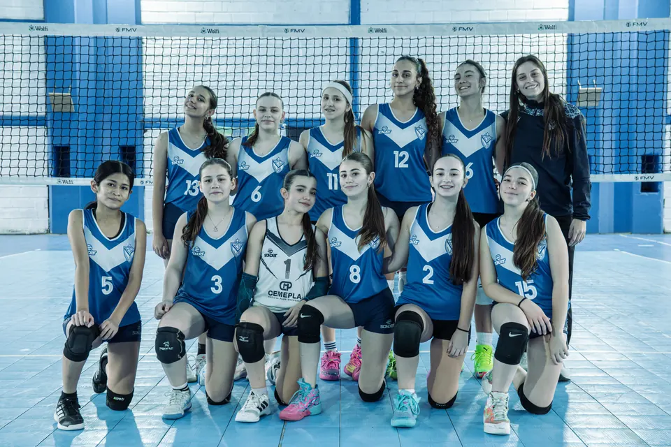 Foto del equipo VELEZ C femenino de la Sub 14 con su entrenadora, frente a la red en el Anexo Alcides Márquez